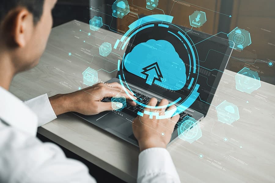 Man on his laptop typing with cloud computing icons in front of him